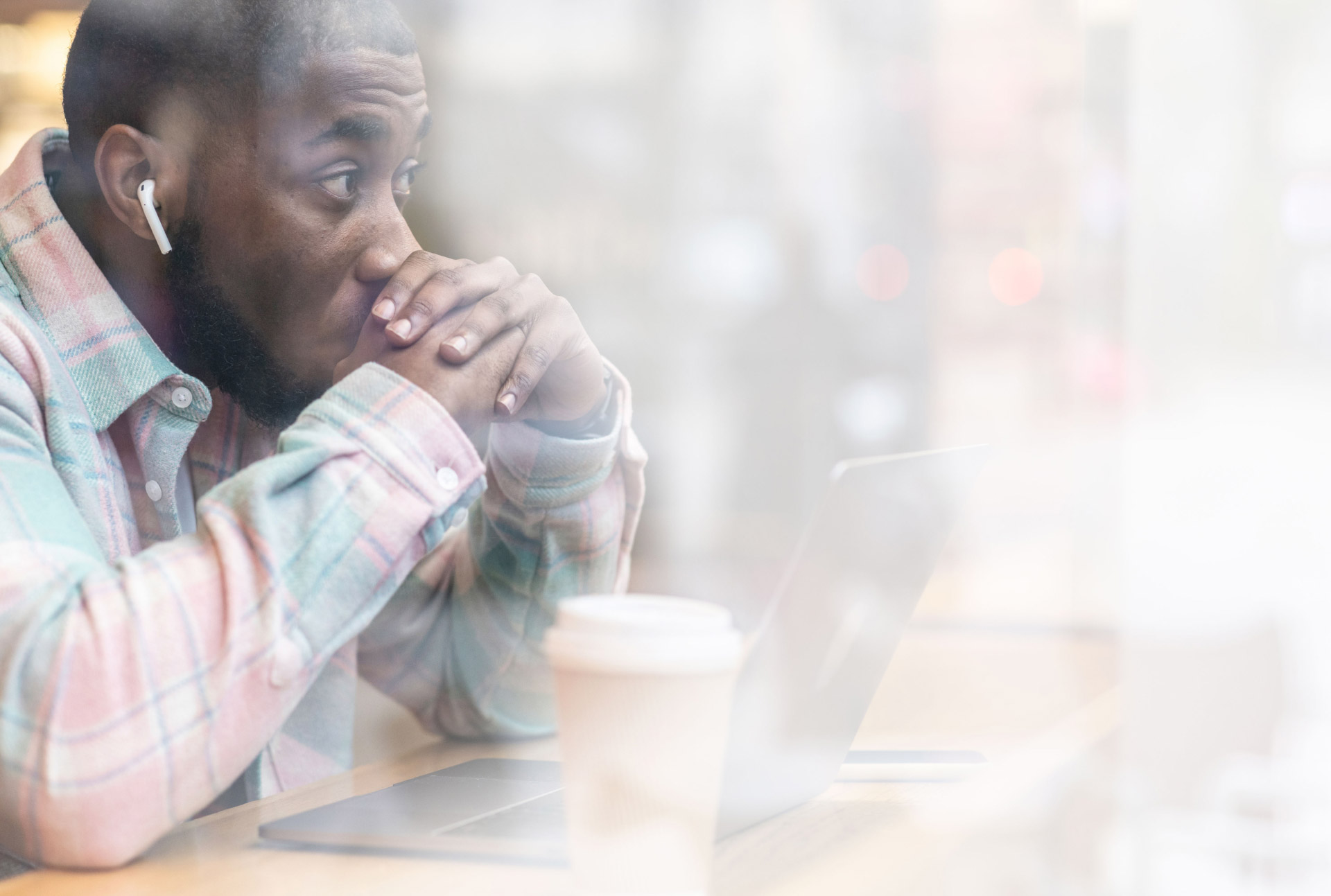 MAN IN CAFÉ WITH HIS LAPTOP, HANDS OVER HIS MOUTH