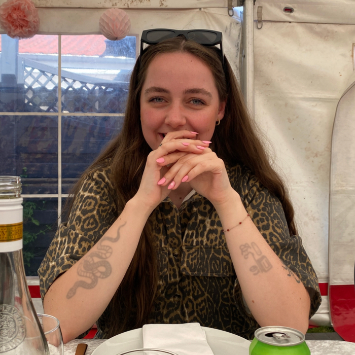 Mia, VYEPTI® patient, sitting at a table with her elbows on table, hands clasped and smiling.